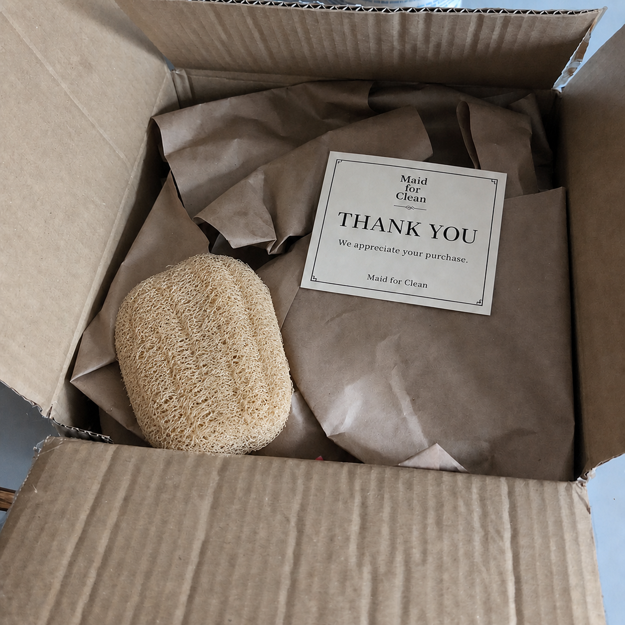 Boxed self-care gift set with body care items, natural loofah, and Maid for Clean thank-you card